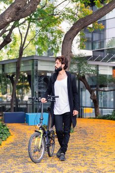 stylish young college student walking with a folding bike in the park of the university campus, concept of youth and education