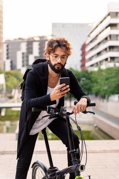 young caucasian man using his mobile phone while sitting on his bike in the city, concept of technology of communication and sustainable mobility