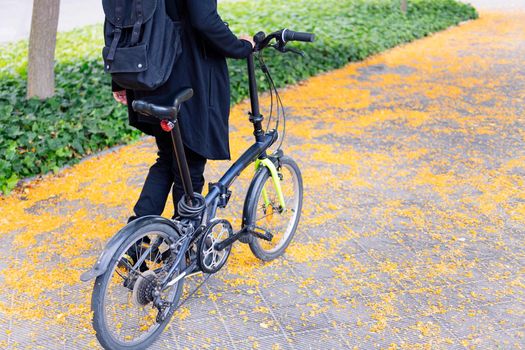 unrecognizable young man with backpack walking with a folding bike on a city park, concept of youth and urban lifestyle, copy space for text