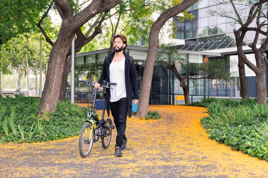 stylish college student walking with a folding bike in the park of the university campus, concept of youth and education, copy space for text