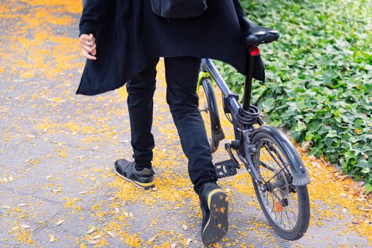 legs of an unrecognizable young man walking with a folding bike on a city park, concept of youth and urban lifestyle, copy space for text