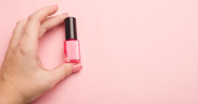 Nail polish in a woman's hand copy space. Article about manicure. Gel polish. Hand care . Pink background