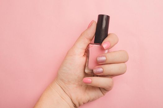 Nail polish in a woman's hand copy space. Article about manicure. Gel polish. Hand care . Pink background