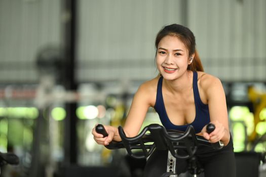 Smiling woman working out on exercise bike in sport gym.