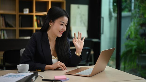Asian businesswoman chatting with colleagues online, video call via computer laptop at her office.