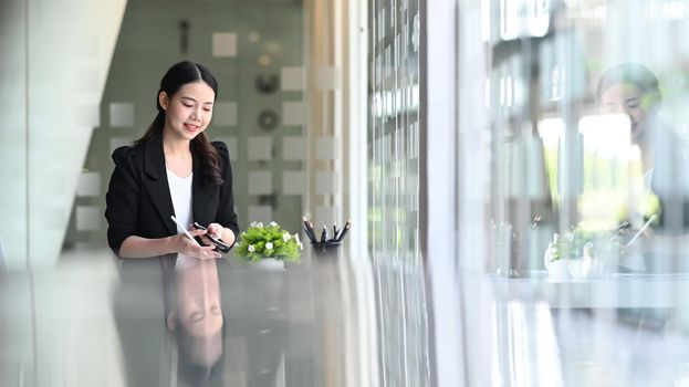 Smiling businesswoman sitting in bright office and using smart phone.