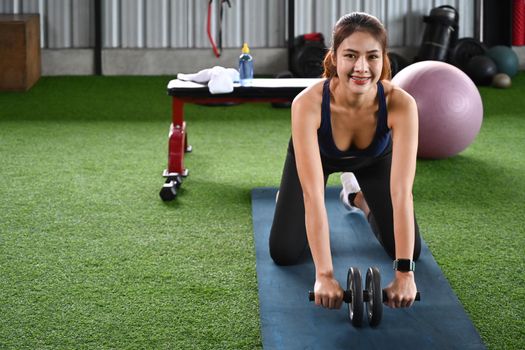 Sporty woman doing exercise with abdominal roller in the gym.