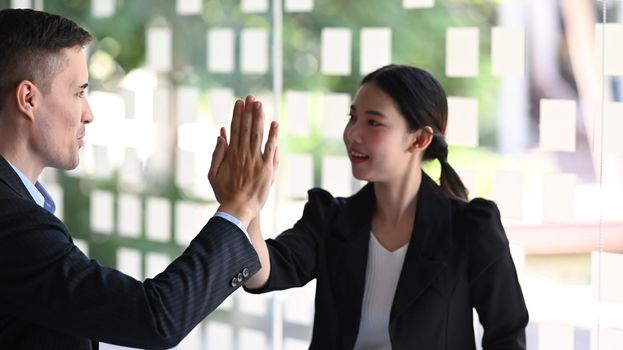 Two smiling business people giving each other high five for celebrating successful work project.
