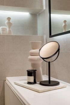 A corner of stylish bathroom with accessories. Detail shot of a table with mirror, candle and ceramic vase. Home decoration concept.