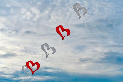 Red and white kites hearts are flying in the wind at the festival of kites