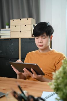 Young man in casual clothes using digital tablet at home.