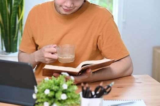 Smiling asian man holding coffee cup and reading book.