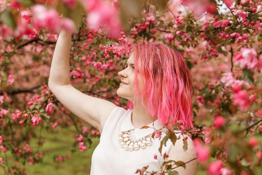 Young girl with pink hair in an Apple orchard. Beautiful young girl in a blooming garden of pink Apple trees.