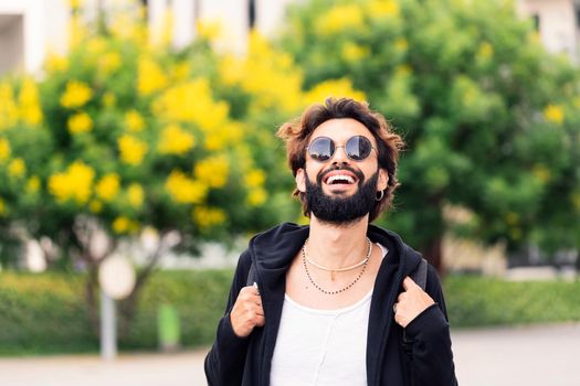 stylish young student with beard and sunglasses laughing happy looking at camera, concept of youth and urban life style, copy space for text