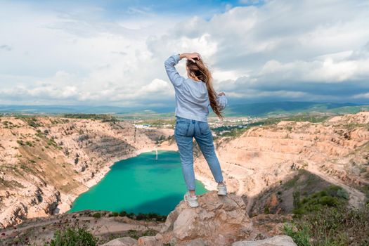 Girl on top of a mountain with raised hands, view of the azure lake in the form of a heart behind.