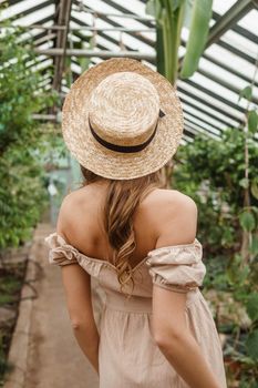 A beautiful young woman takes care of plants in a greenhouse. The concept of gardening and an eco-friendly lifestyle.