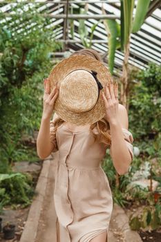 A beautiful young woman takes care of plants in a greenhouse. The concept of gardening and an eco-friendly lifestyle.