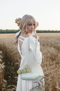 A blonde woman in a long white dress walks in a wheat field. The concept of a wedding and walking in nature.