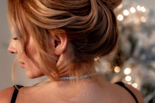 Portrait of a wealthy mature woman with evening makeup and hairstyle posing in a black dress against the backdrop of a Christmas room. Luxurious lifestyle. Cosmetology, plastic surgery, rejuvenation