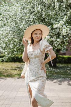 An attractive long-haired woman walks in the spring in the park of blooming apple trees. Spring portrait of a woman