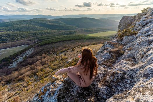 A girl sits on the edge of the cliff and looking at the sun valley.Woman enjoying a sunset or sunrise from the top of the mountain in summer.The traveler girl see the sunrise at the peak of mountain