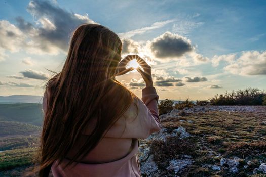 The girl made a beautiful heart from her finger in the rays of the sun. healthy woman making heart shape with hands at sunset. Shining summer sun on your hands. healthy heart concept