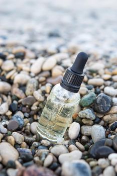 Cosmetic serum for the skin in a glass bottle. A bottle with an eyedropper on a pebble beach by the sea. Essences for skin care on the background of stones. The concept of natural cosmetics and SPA products.