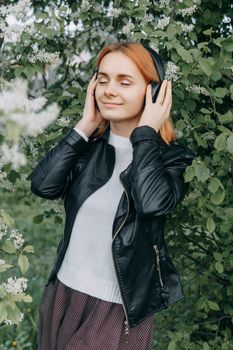 A red-haired teenage girl listens to music in headphones, configured via the phone. The time of spring flowering of cherry orchards