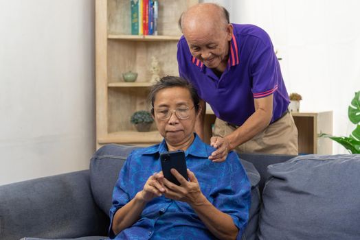 Asian senior holding mobile smart phone communication online internet video call together on sofa at home.