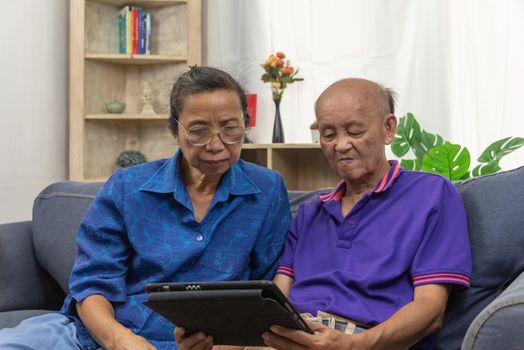 Asian senior using tablet online internet communication technology on sofa at home.