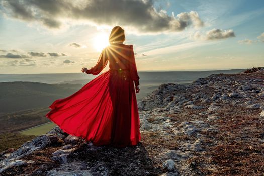 Rise of the mystic. sunset over the clouds with a girl in a long red dress. Stands on the mountain with a magical view