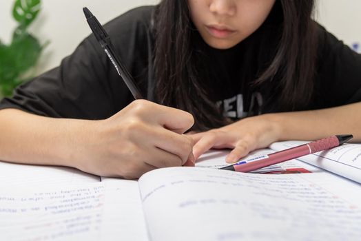 Asian student girl is writing homework and reading book at desk