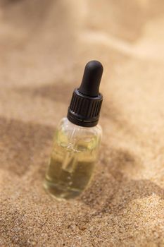 Cosmetic serum for the skin in a glass bottle. A bottle with a pipette on a sandy beach by the sea. Essences for skin care on a sandy background. The concept of natural cosmetics and SPA products.