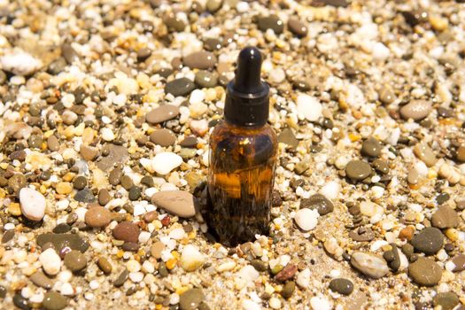 Cosmetic serum for the skin in a glass bottle. A bottle with an eyedropper on a pebble beach by the sea. Essences for skin care on the background of stones. The concept of natural cosmetics and SPA products.