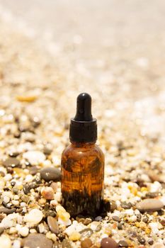 Cosmetic serum for the skin in a glass bottle. A bottle with an eyedropper on a pebble beach by the sea. Essences for skin care on the background of stones. The concept of natural cosmetics and SPA products.