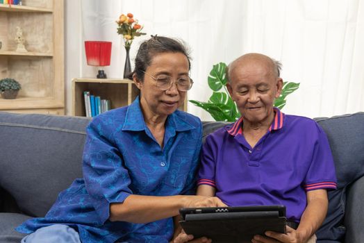 Asian senior using tablet online internet communication technology on sofa at home.
