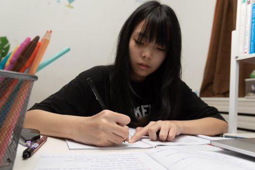 Asian student girl is writing homework and reading book at desk