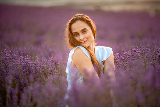 A beautiful girl in a white dress and loose hair on a lavender field. Beautiful woman in a lavender field at sunset. Soft Focus.