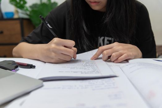 Asian student girl is writing homework and reading book at desk