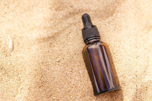 Cosmetic serum for the skin in a glass bottle. A bottle with a pipette on a sandy beach by the sea. Essences for skin care on a sandy background. The concept of natural cosmetics and SPA products.