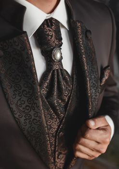 Luxurious modern expensive brown wedding men's suit with an abstract pattern and pearls on a tie with a white shirt.