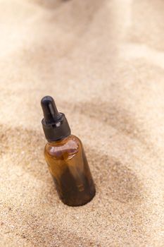 Cosmetic serum for the skin in a glass bottle. A bottle with a pipette on a sandy beach by the sea. Essences for skin care on a sandy background. The concept of natural cosmetics and SPA products.