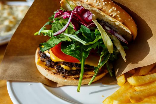 Big burger with beef cutlet and salad in a paper envelope