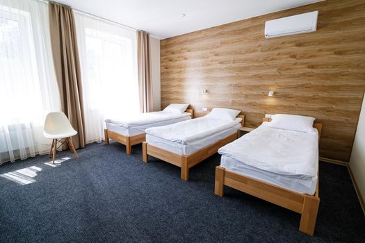 Large bright room in a hostel with three beds. White bedding