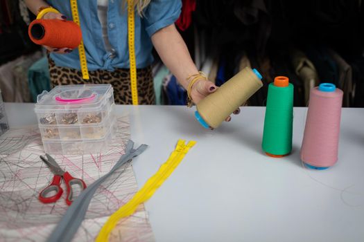 A blonde woman at a tailor shop is trying to choose the right thread color for her next blouse. A women's clothing designer.
