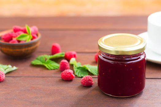 fresh raspberry jam in a glass jar on a wooden table, next to fresh raspberries. concept of homemade jam, preserves for winter, selective focus.