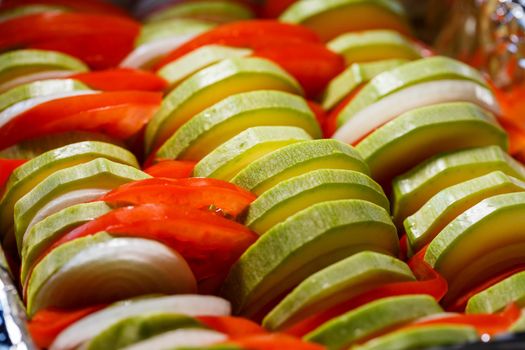 chopped vegetables tomatoes, zucchini, onions, peppers folded into a baking dish. Cooking ratatouille