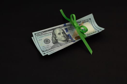 American cash money, banknotes of us dollars tied with green ribbon on black background, one hundred dollar bills in stack