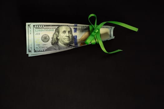 American cash money, banknotes of us dollars tied with green ribbon on black background, one hundred dollar bills in stack