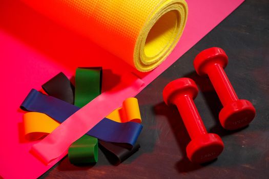 Red dumbbells, fitness mat and elastic bands for sports on a pink background. Healthy lifestyle. Fitness equipment for weight training. Muscle development and fitness training